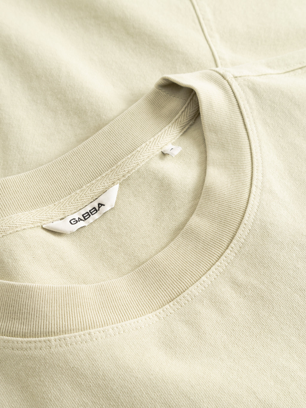 Close-up of the Gabba GABnigel Wix Boxy Hour SS t-shirt in Alfa Green, neatly folded to highlight its heavyweight cotton crew neck and visible white tag. The boxy fit and fabric look soft and smooth.