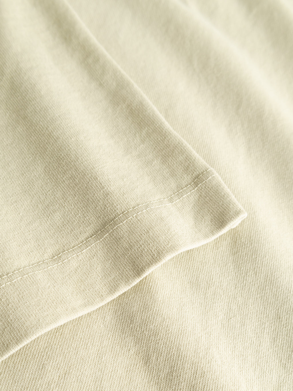 Close-up of the GABnigel Wix Boxy Hour SS in Alfa Green by Gabba, showcasing heavyweight cotton fabric with a visible hem and neat double-stitched seams. The texture and weave of the soft material are clearly shown.