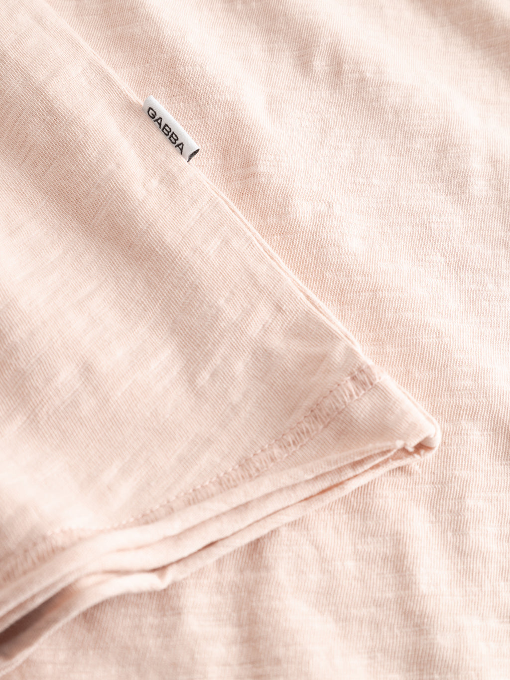 A close-up of the Gabba GABkostant New SS t-shirt in Misty Rose shows its textured, slub 100% cotton fabric and a small white Gabba tag sewn into the seam.