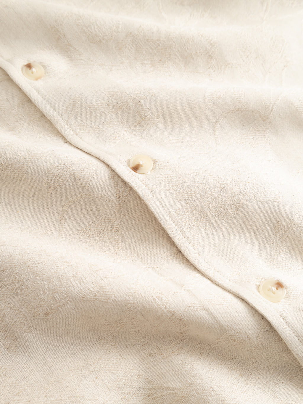 Close-up of Gabba's GABjens Over Resort Soft SS Shirt in Ecru: cream-colored, textured linen blend fabric with a subtle pattern and glossy, round buttons along the seam—ideal for an oversized shirt look.