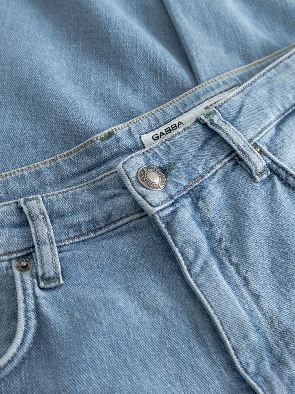 Close-up of GABmarc Hobok Jeans in mid blue denim by Gabba, featuring visible stitching, a metal button, belt loops, and a white brand label.