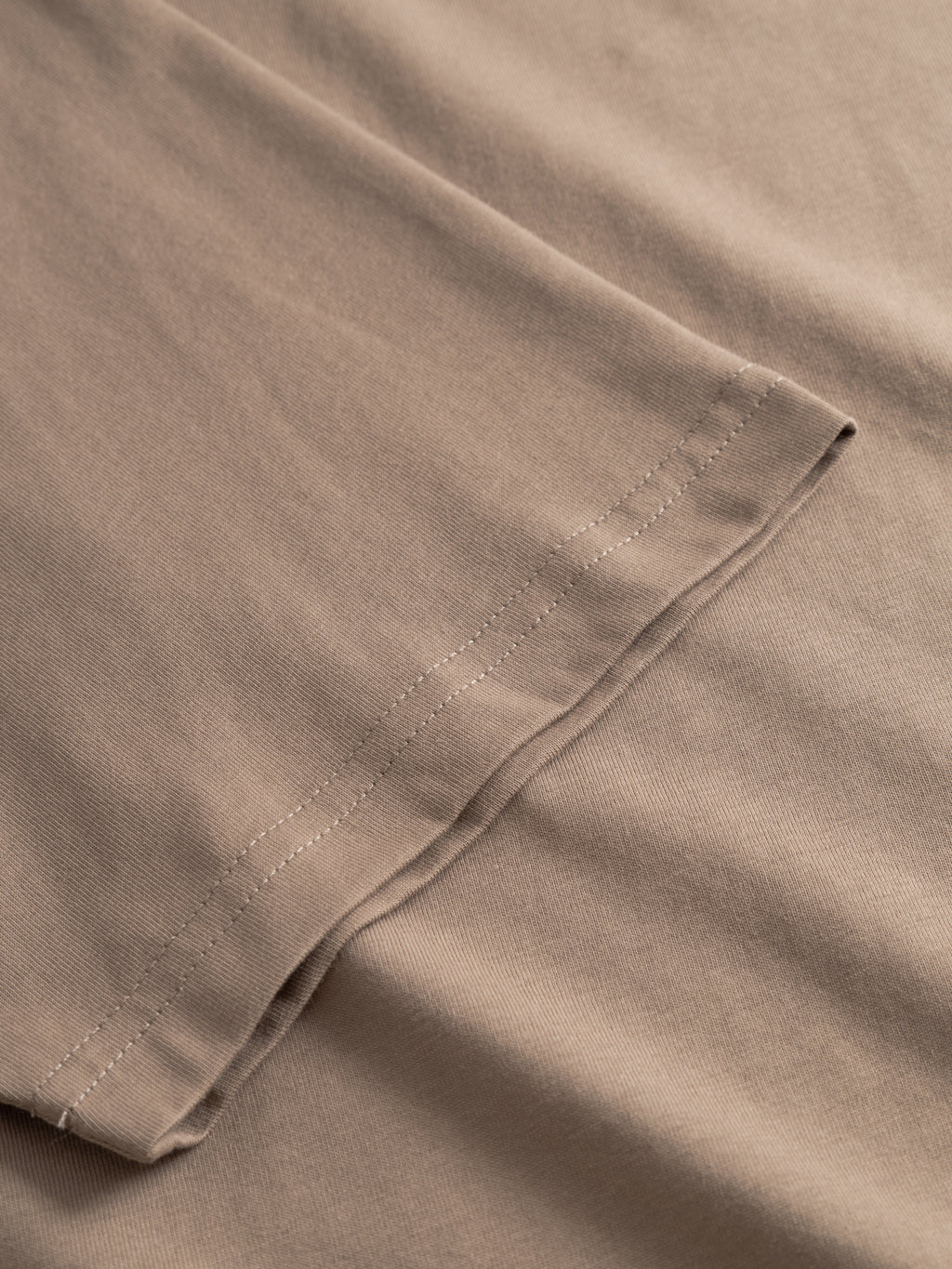 A close-up of the hem of the Gabba GABdune Logo GOTS SS T-Shirt in Fungi, showcasing the organic cotton fabric’s texture and detailed stitching.