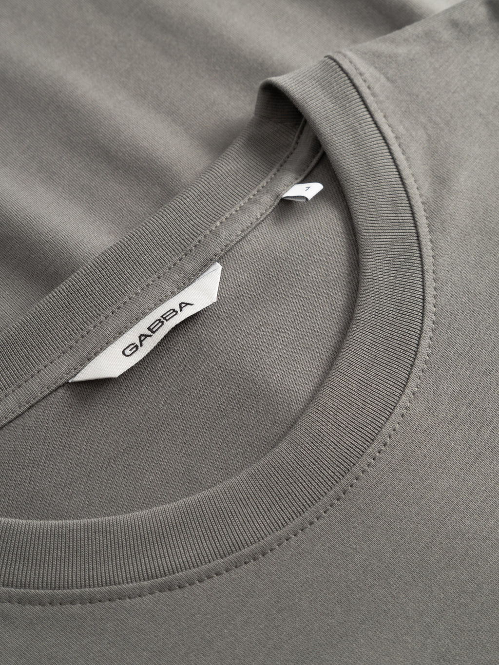 Close-up of a GABdune Logo GOTS SS T-Shirt in Castor Gray, highlighting classic fit, detailed stitching, and a white collar label featuring the Gabba brand name in black.