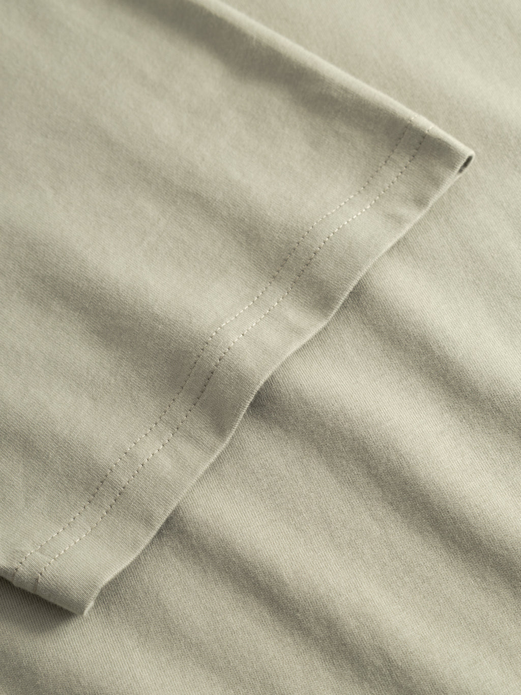 A close-up of the hem on the Gabba GABdune Logo GOTS SS T-Shirt in light green, showing the fabric texture and precise double-stitched seams.