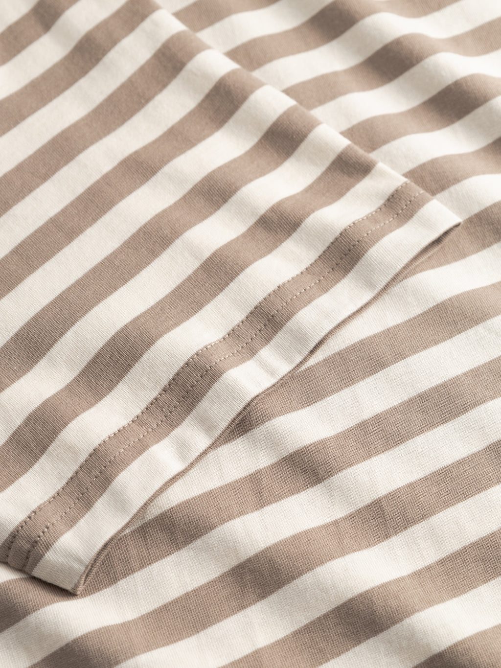 Close-up of Gabba’s GABdune Logo Stripes SS GOTS - Fungi tee, featuring beige and white horizontal stripes in organic cotton with intersecting seams and soft knit texture.