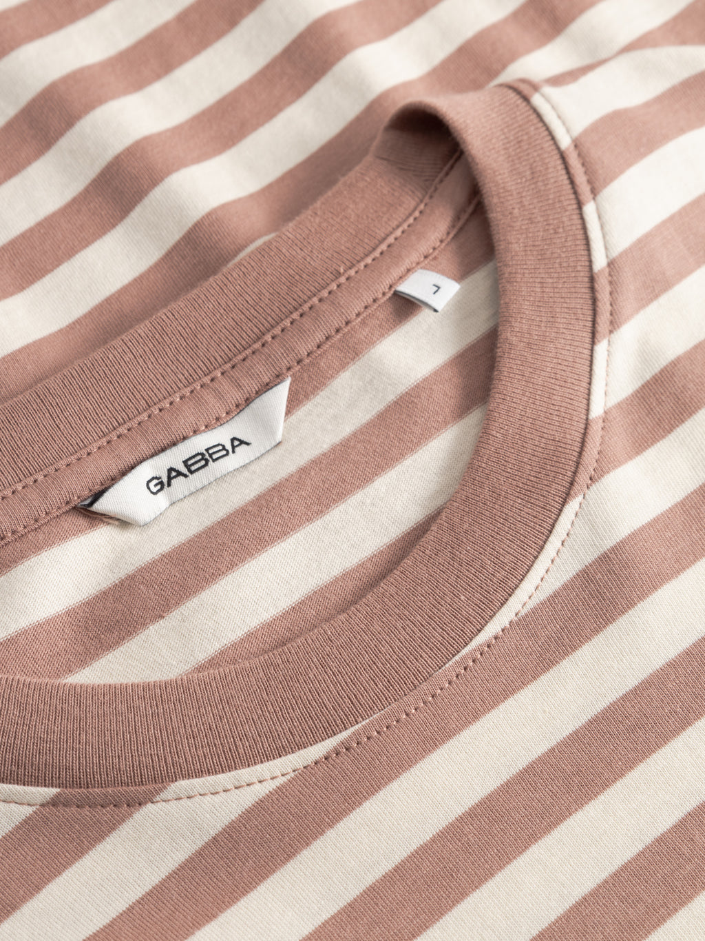 Close-up of the GABdune Logo Stripes SS GOTS t-shirt in wood pink, featuring beige and white stripes. The neckline reveals a sewn-in Gabba brand label and a small size tag marked Z. Made from organic cotton.