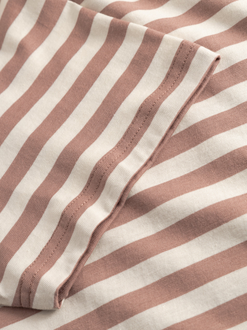 A close-up of the Gabba GABdune Logo Stripes SS GOTS - Wood Pink t-shirt shows soft organic cotton fabric with beige and light brown horizontal stripes, folded edges, and visible stitching.