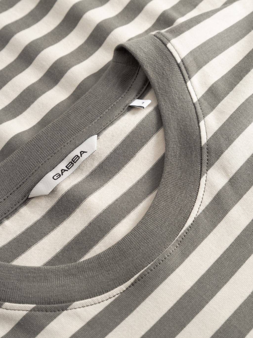 Close-up of the GABdune Logo Stripes SS GOTS t-shirt in Castor Gray by Gabba, featuring gray and white stripes, a classic crew neck collar, and a visible inside label with the Gabba brand name.