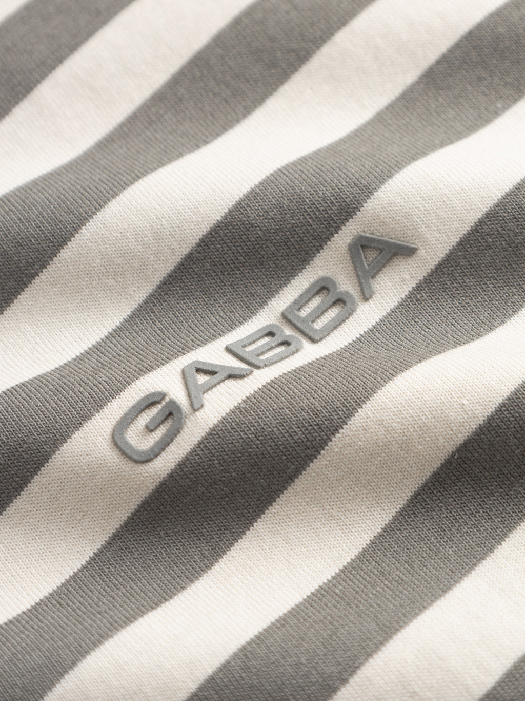 Close-up of the Gabba GABdune Logo Stripes SS GOTS t-shirt in Castor Gray, made from GOTS-certified organic cotton with gray and white stripes, featuring raised silver 
