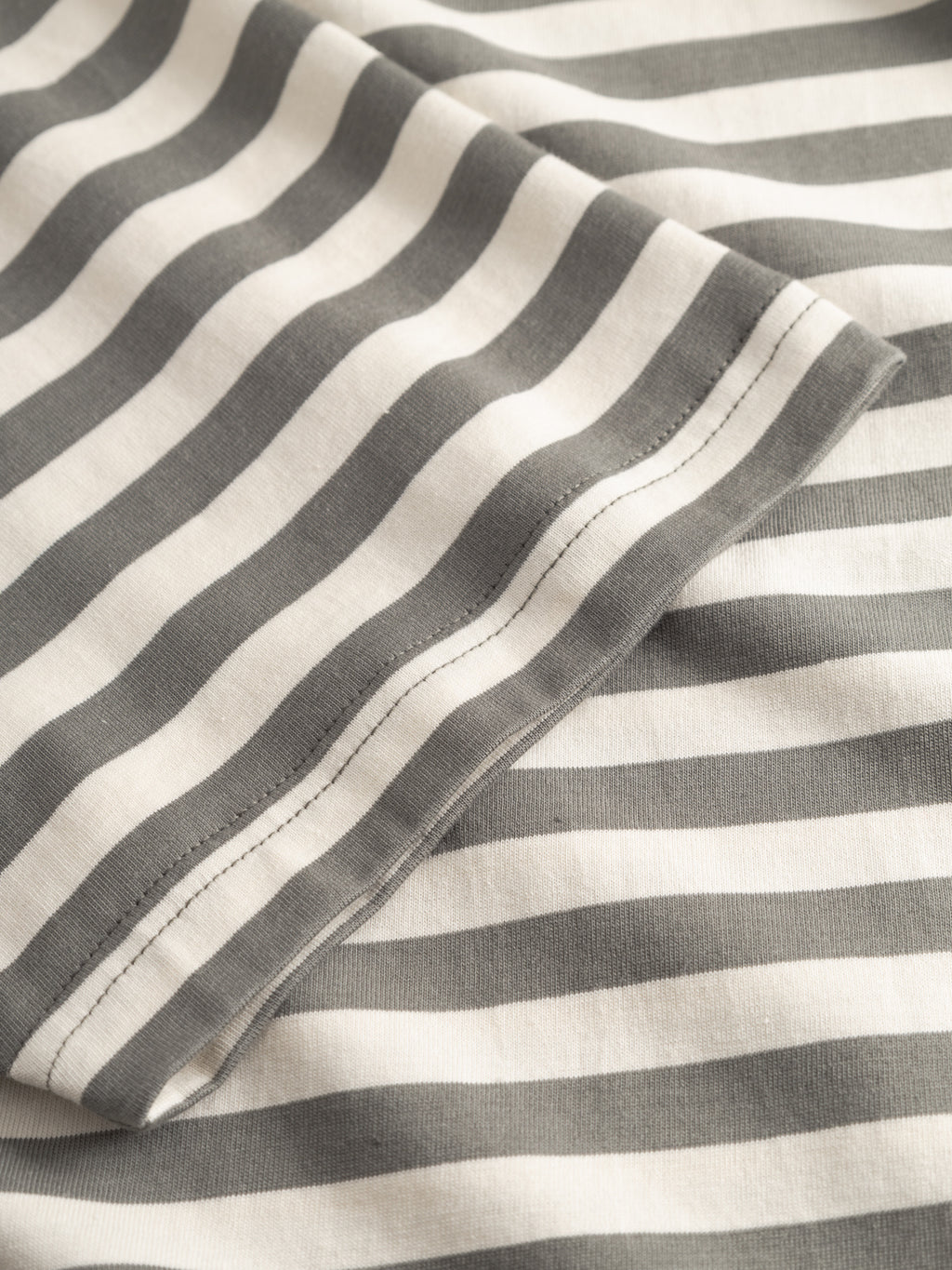 Close-up of the Gabba GABdune Logo Stripes SS GOTS t-shirt in Castor Gray, showing horizontal gray and white stripes, soft GOTS-certified organic cotton fabric, and visible stitching on a folded edge.