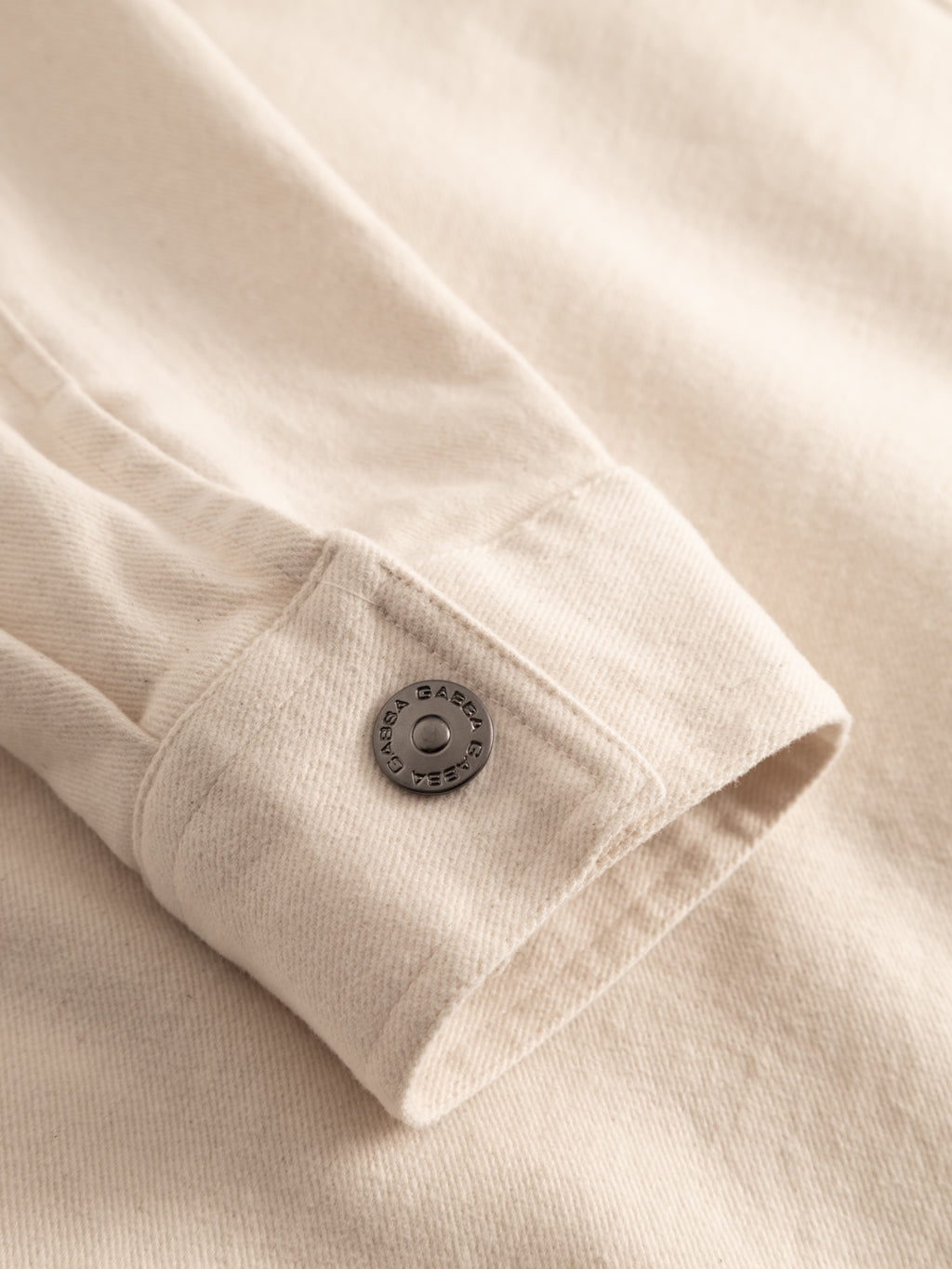 Close-up of a Gabba GABbeta Twill - Ecru overshirt sleeve featuring a metal engraved button at the cuff, showcasing the textured twill fabric.