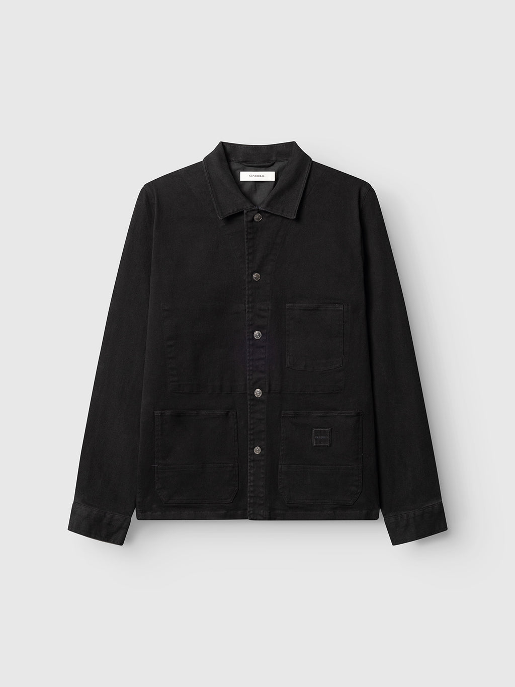 The Gabba GABbeta Twill - Black is a black garment dyed twill workwear overshirt with long sleeves, a collar, and large front pockets, shown on a plain light gray background.