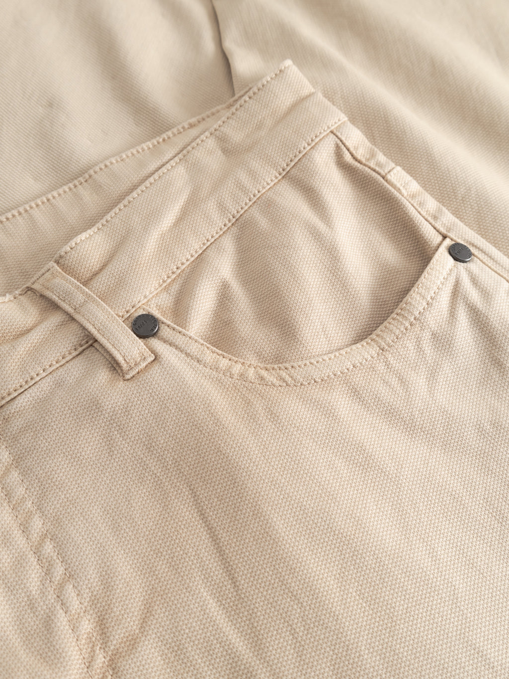 Close-up of the front pocket and waistband of the Gabba GABmarc 5poc Marlo - Birch jeans, highlighting stitching, a belt loop, and metal rivets. The subtly textured beige fabric makes these regular-fit jeans comfortable for everyday wear.