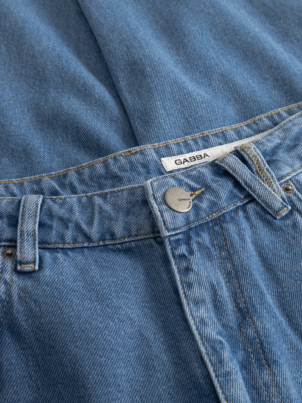 A close-up of Gabba GABmarc 5poc Mid Jeans in Mid Blue Denim shows the metal button, belt loops, classic 5-pocket design, and a white Gabba label above the waistband.