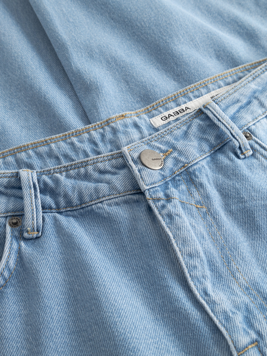 Close-up of Gabba’s GABmax 5poc Lig Jeans in light blue denim, made from 100% cotton with visible button, belt loop, brand label on the waistband, and 5-pocket style, laid flat on matching denim.
