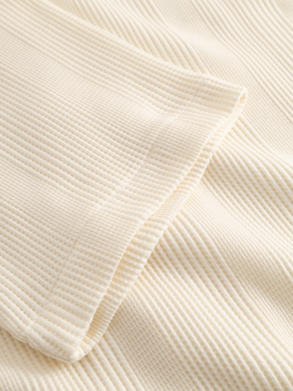 Close-up of the Gabba GABvalente Wup SS T-Shirt in Bone White, featuring an off-white ribbed texture with vertical lines and a folded edge. The soft, slightly elastic fabric ensures comfort, perfect for relaxed-fit clothing.