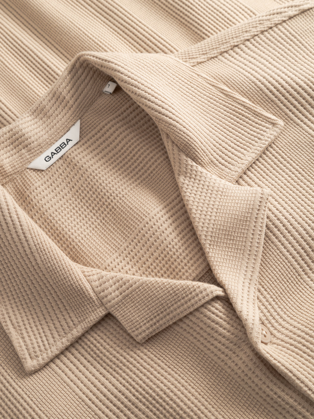 Close-up of Gabba’s GABvalente Wup SS T-Shirt in Humus, featuring a beige waffle texture, resort collar with folded lapel, and a white “Gabba” label sewn inside the neckline.