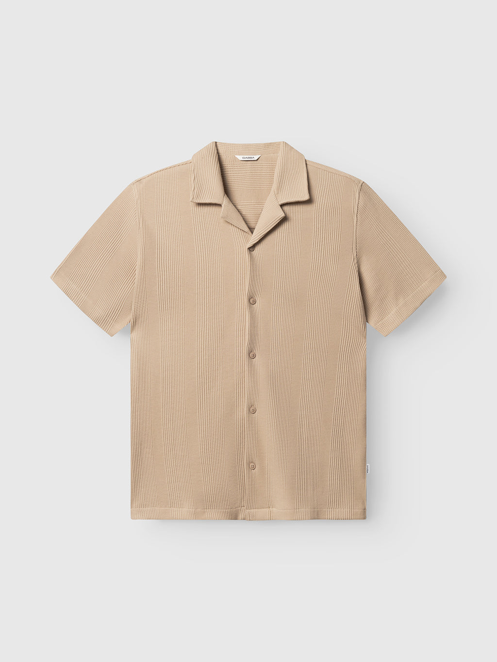 The Gabba GABvalente Wup SS T-Shirt in Humus is a beige, relaxed fit shirt with short sleeves, a resort collar, and subtle vertical textured lines, displayed on a plain white background.