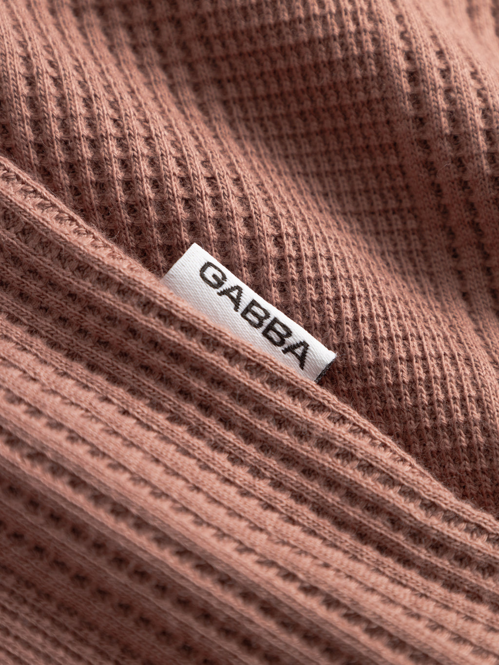 A close-up of the Gabba GABvalente Wup SS T-Shirt in Wood Pink shows its waffle texture and a small white seam tag with 