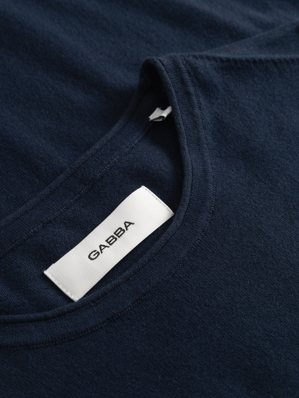 Close-up of the GABlima Cot LS Knit - Navy t-shirt by Gabba, featuring seamless detailing and a white neck label with the brand name 