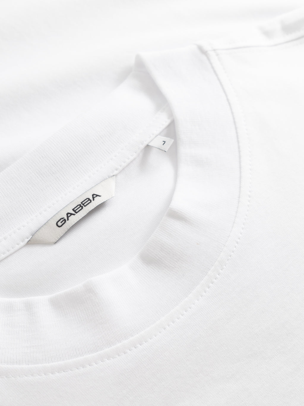 Close-up of a Gabba GABnigel Boxy NBH SS T-shirt GOTS in white, highlighting the neckline and inner tag. The tag shows 