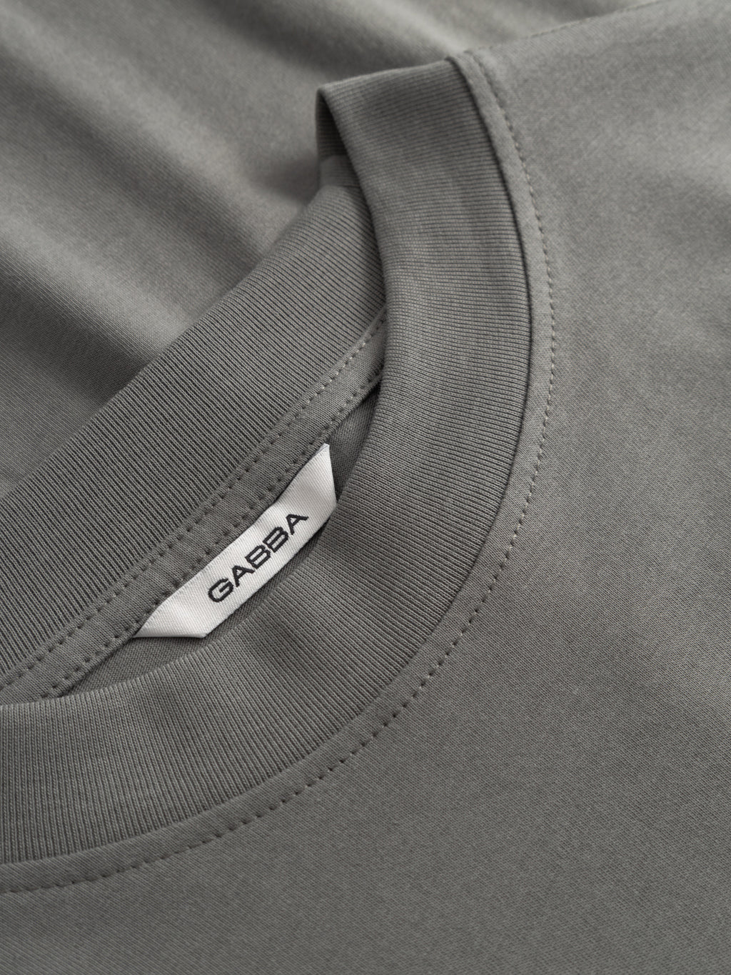 Close-up of the GABnigel Boxy NBH SS T-shirt GOTS in Castor Gray by Gabba, featuring an oversized fit, ribbed crew neckline, and a white inner collar tag with the Gabba brand name in black letters.