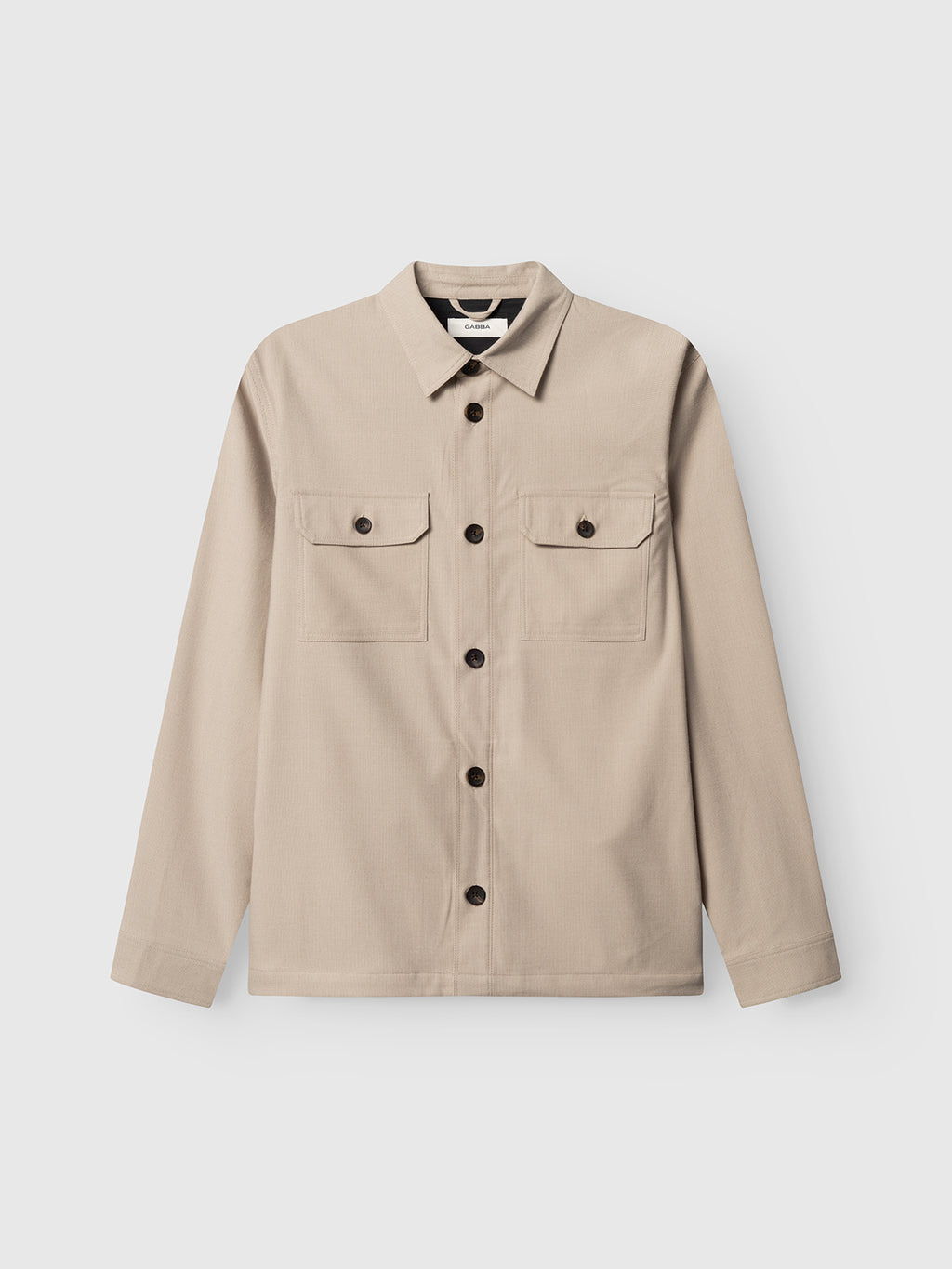 The Gabba GABtogger Base Deme LS Overshirt in Birch is a beige, long-sleeve button-up shirt with a collar and two chest pockets with buttoned flaps, shown on a plain white background.