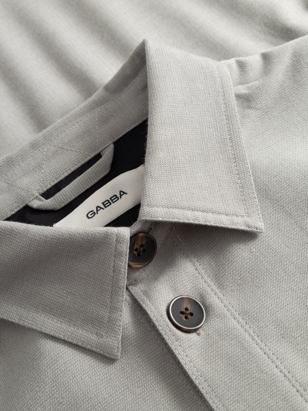 Close-up of the Gabba GABtogger Base Deme LS Overshirt in Mineral Gray, showing two buttons and the white brand label inside the collar—refined details make this shirt a standout for your next style test.