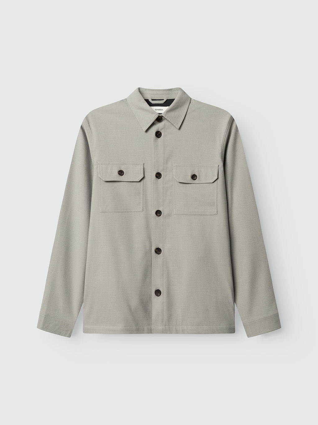The Gabba GABtogger Base Deme LS Overshirt in Mineral Gray is a light grey, long-sleeve button-up with a collar, dark buttons, and two front chest pockets with flap and button closures; it features a minimal design.
