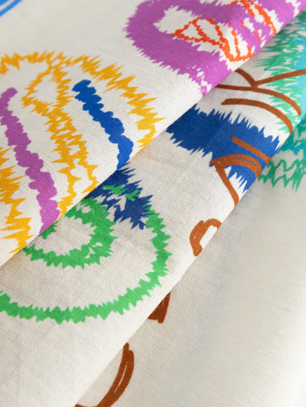 Close-up of the GABnando Bandana - Multi Pattern by Gabba, showing its soft cotton blend fabric with colorful abstract zigzag and swirl designs in yellow, blue, purple, green, brown, and red on overlapping folds.