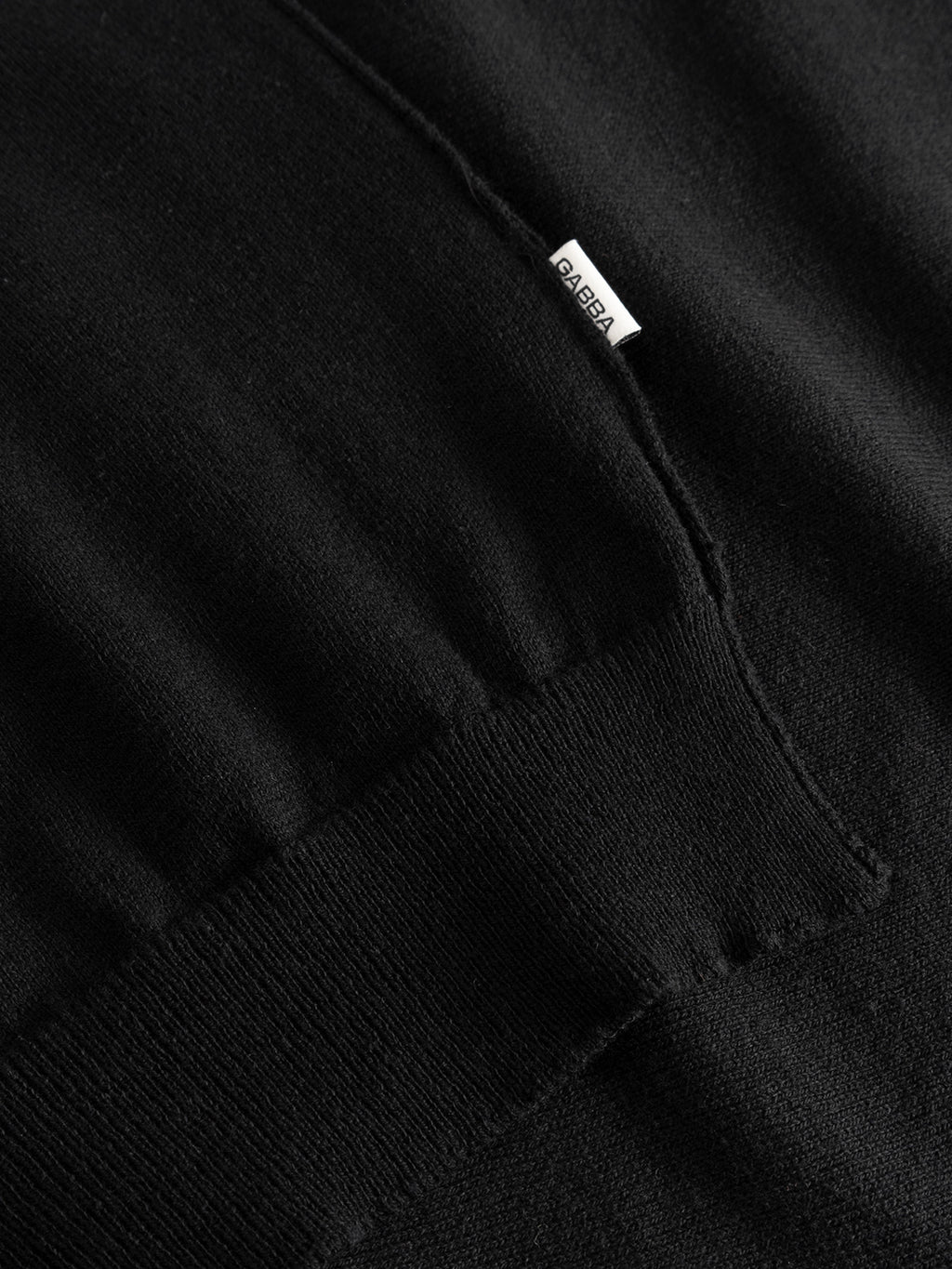 Close-up of Gabba's GABfumo Spy LS Knit in black, a regular-fit knit garment featuring a ribbed cuff or hem and a small white tag.