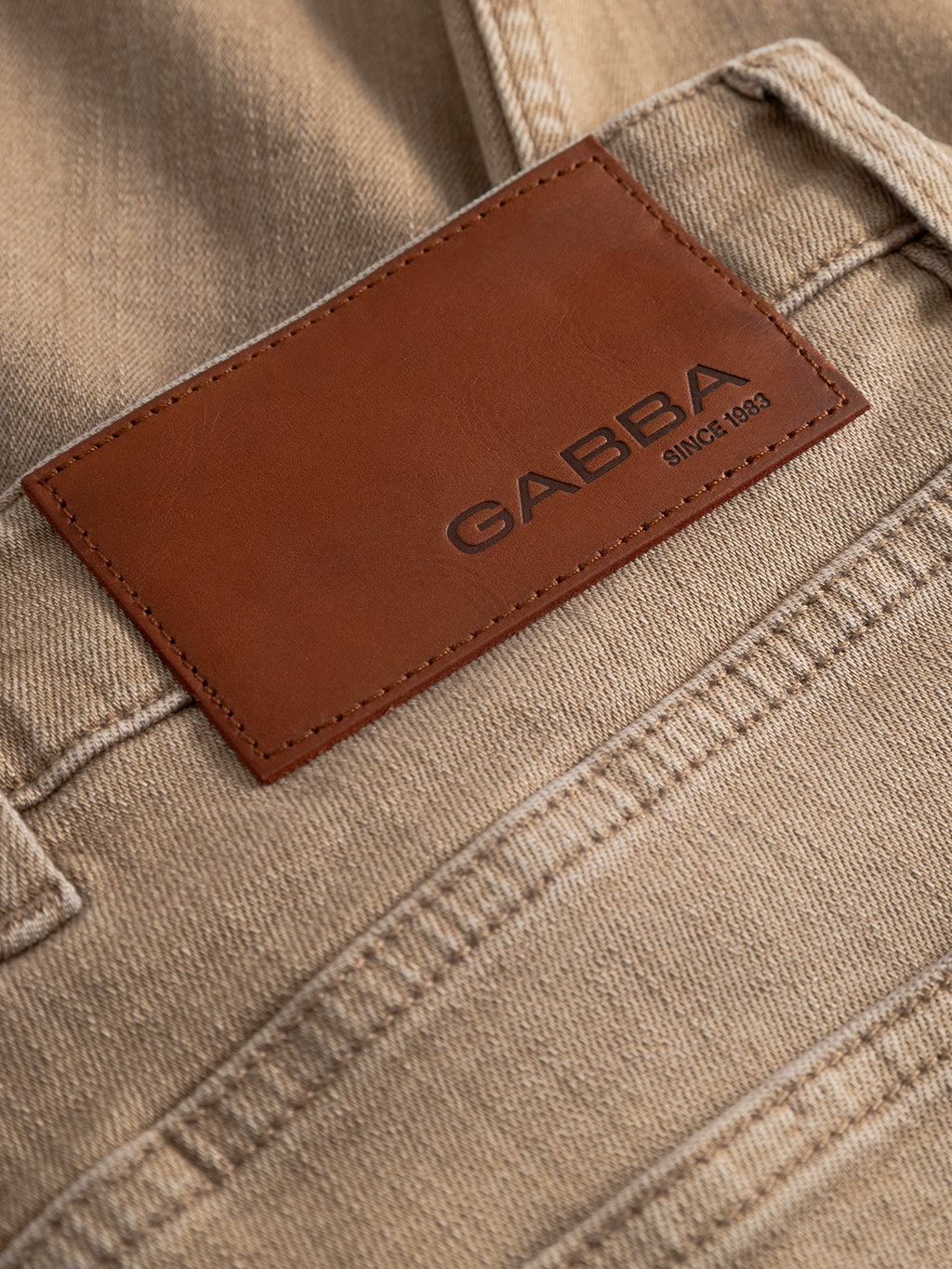 Close-up of sand denim fabric with a brown leather patch reading 