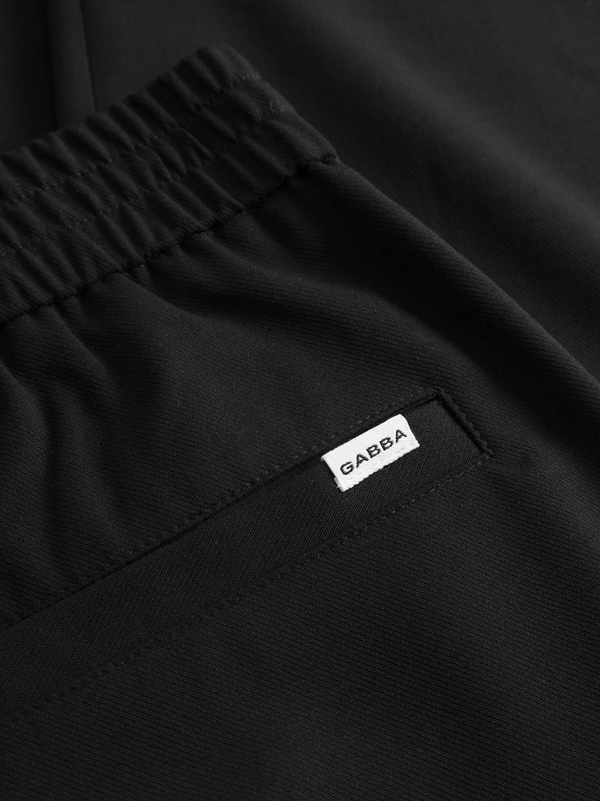 Close-up of the GABnapoli 19 Phin GRS - Black by Gabba, a black wool blend chino featuring an elastic waistband and a pocket adorned with a small white label reading “GABBA.” This garment offers a regular straight fit for effortless style and comfort.