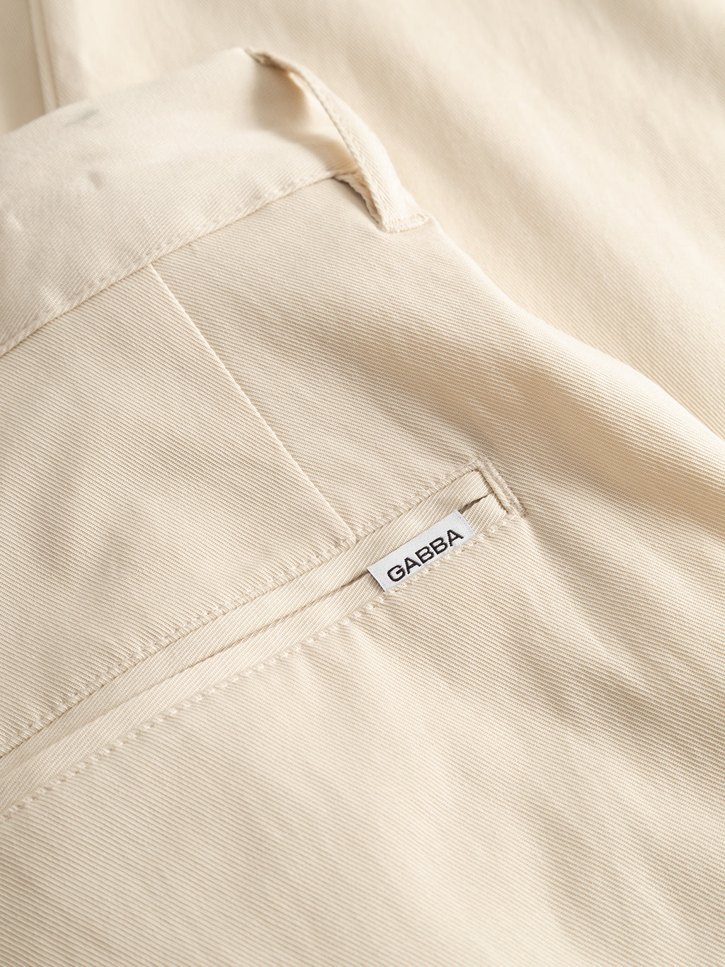Close-up of the GABfirenze Bolu Cropped TENCEL™ Pant in Birch by Gabba, featuring cream-colored, relaxed-fit fabric with a fine diagonal weave and a back pocket with a small white Gabba label.