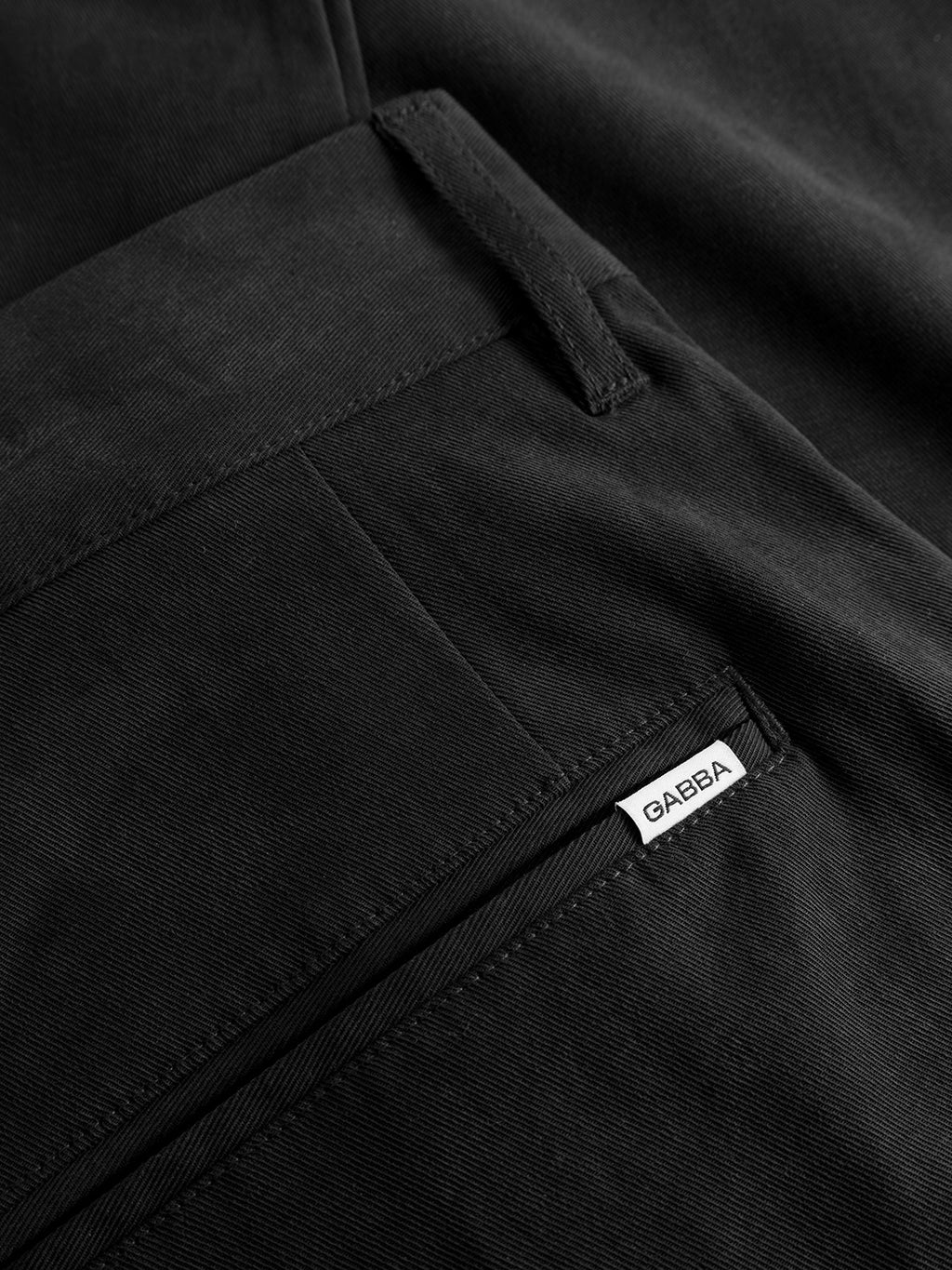 Close-up of the GABfirenze Bolu Cropped TENCEL™ Pant in black by Gabba, highlighting the back pocket with a small white fabric tag labeled “Gabba.” Made from smooth, finely woven stretch twill, these pants offer a relaxed fit for all-day comfort.