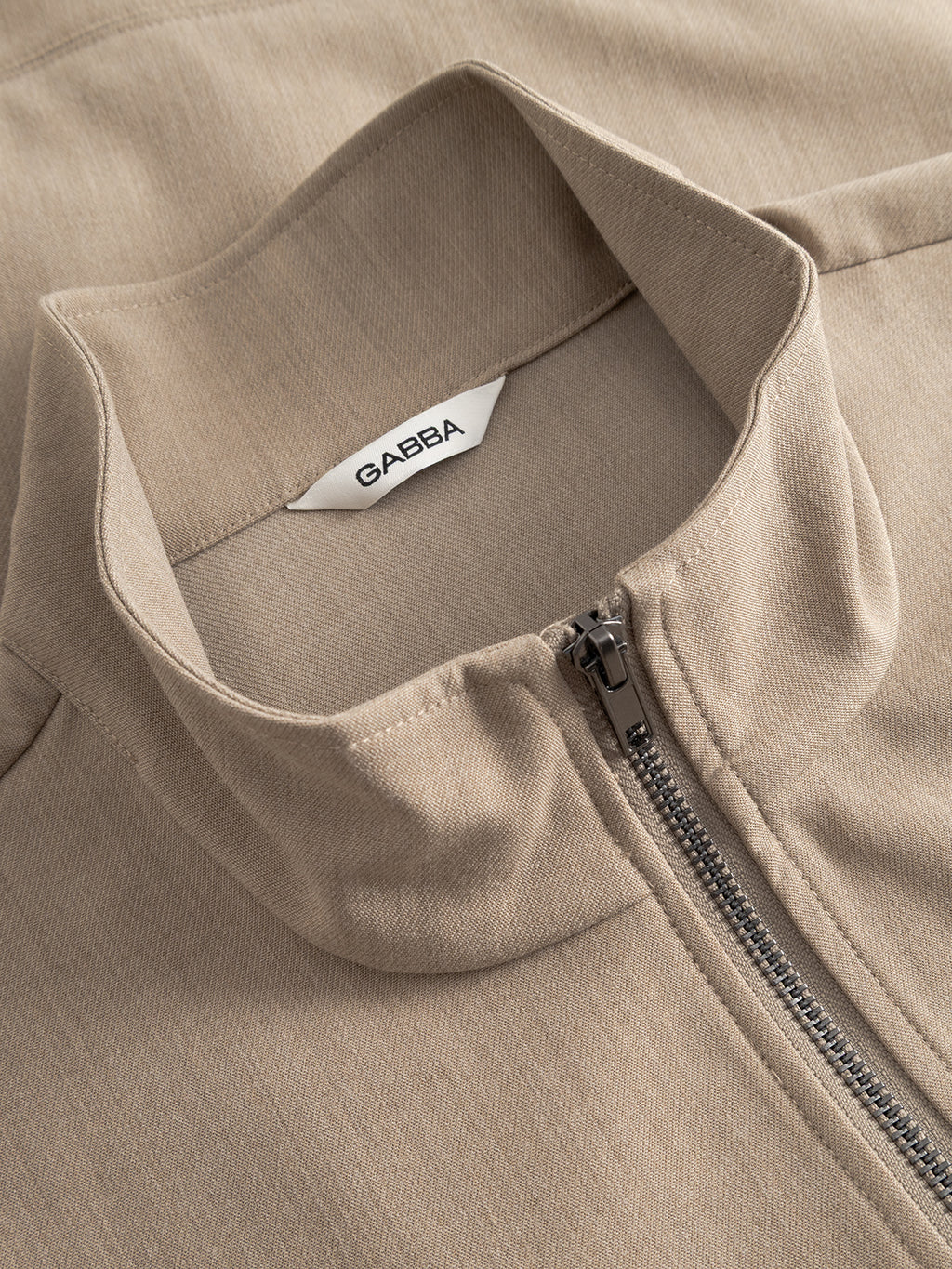 Close-up of the Gabba GABnik Phin GRS - Sand Plaza jacket with a standing collar and white inner label. This regular fit beige zip-through is crafted from soft, textured fabric for comfort.