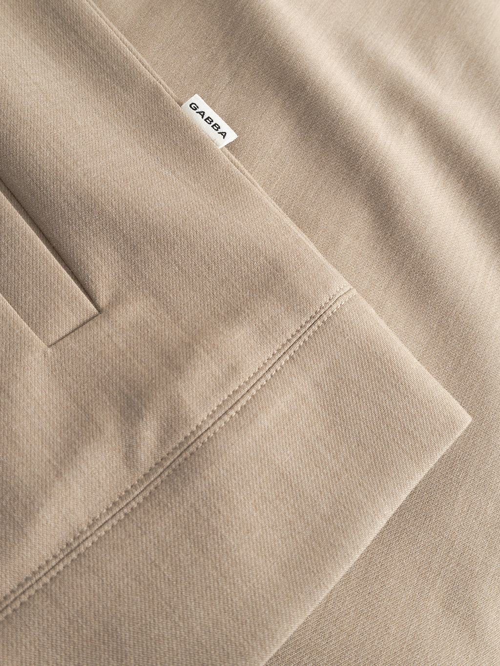 Close-up of Gabba’s GABnik Phin GRS - Sand Plaza beige pants with a small white label by the side pocket, showcasing textured fabric and fine stitching—ideal to style with your favorite regular fit jacket.