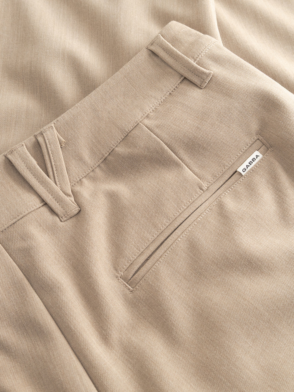 Close-up of Gabba GABfirenze Phin Cropped GRS - Sand Plaza trousers highlighting the waistband, belt loops, and welt pocket with a white Gabba label. The soft, slightly textured fabric adds to their versatile style.
