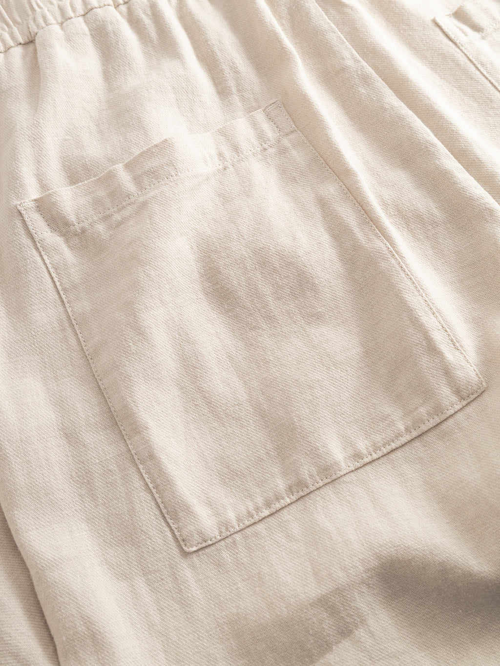 Close-up of the Gabba GABzeta Lino - Birch: a beige linen garment featuring a rectangular patch pocket and gathered waistband. The breathable fabric highlights its comfort and style.