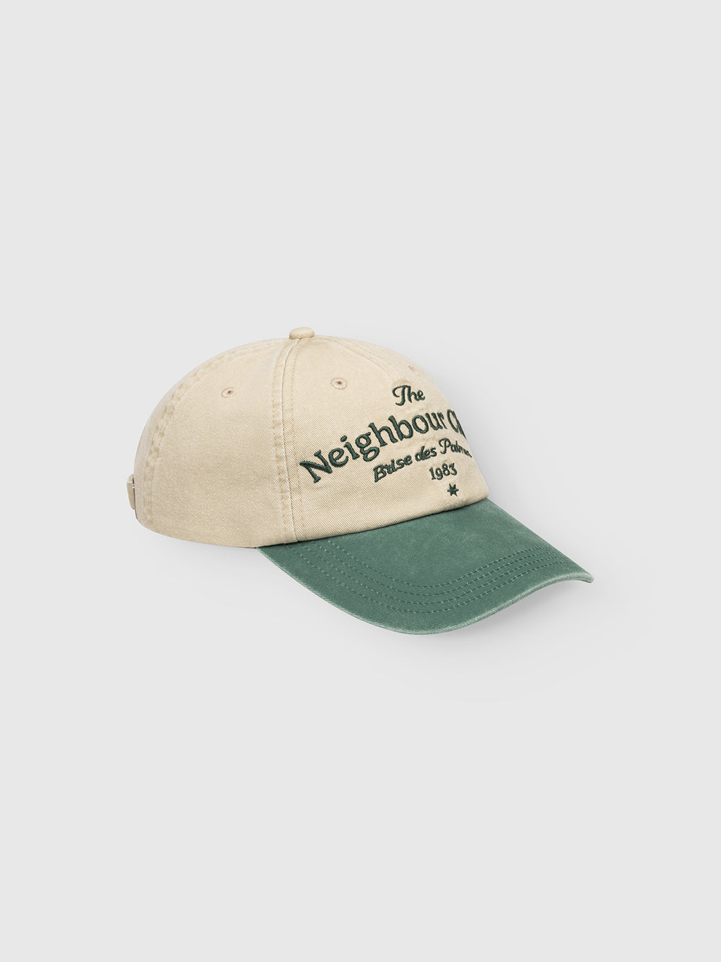 The Gabba GABnbh Club Cap - Green is a beige, regular-fit cap with a green curved brim and green “The Neighbour Brise des Pubs 1985” embroidery. Made from soft material, it features a subtle Gabba logo on a light background.