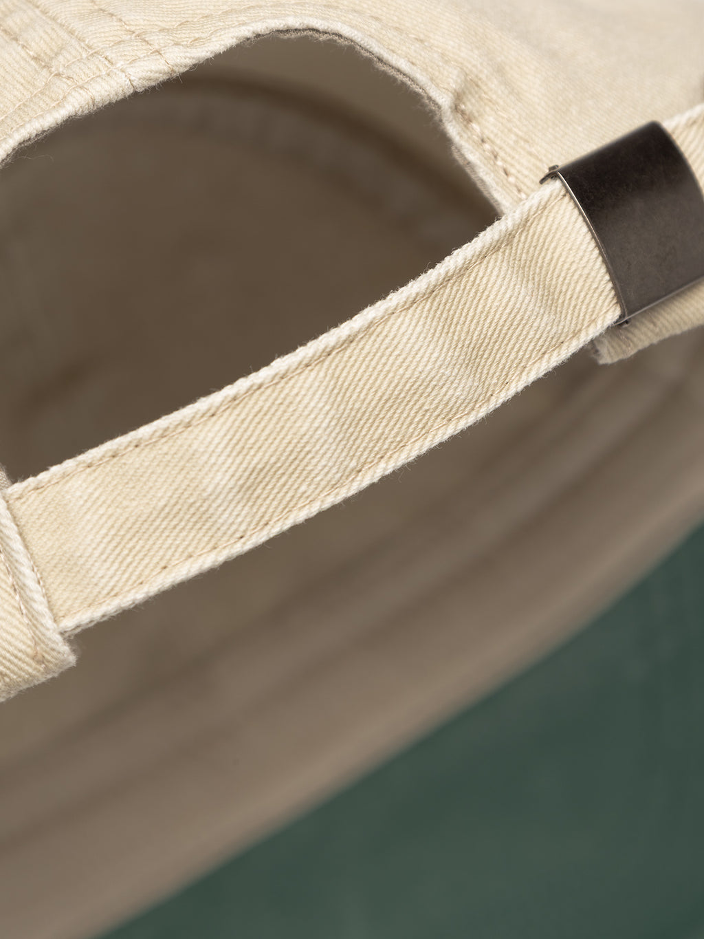 Close-up of the adjustable strap and metal clasp on the Gabba GABnbh Club Cap - Green, crafted from soft material, shown against a blurry green background.