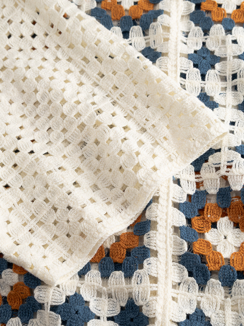 Close-up of the Gabba GABcrochet Pattern SS Knit - Multi Pattern: a solid off-white crochet layering piece over a white, blue, and rust orange granny square design.