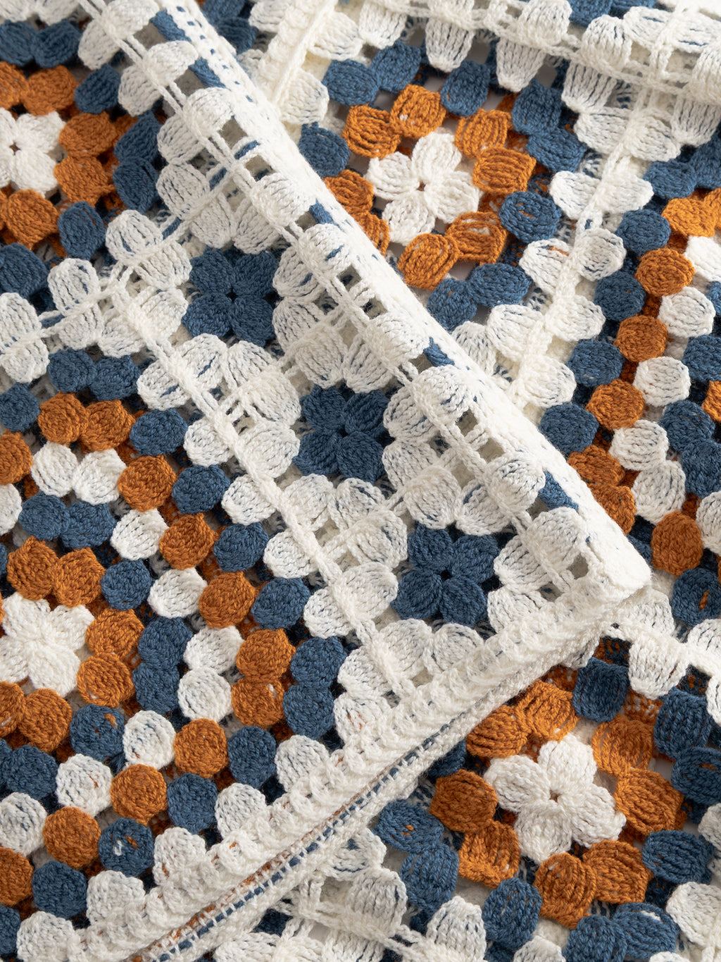 A close-up of the Gabba GABcrochet Pattern SS Knit - Multi Pattern, in blue, white, and orange yarn. The textured stitches and layered design highlight its versatility as a cozy, stylish crochet blanket.