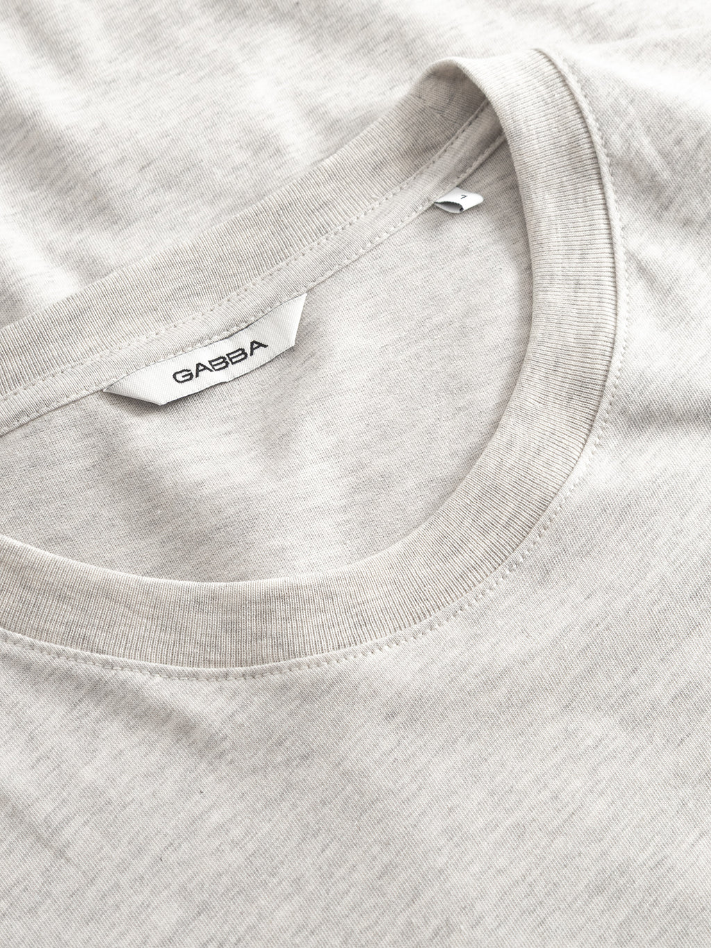 Close-up of a GABdune Melange New SS T-Shirt in Lt. Grey Mel by Gabba, highlighting the collar and inner white brand label. The jersey fabric looks soft with a subtle texture for a comfortable feel.