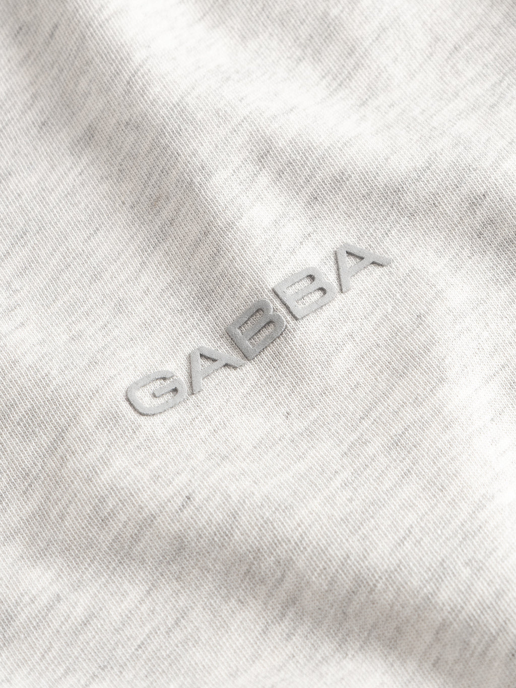 Close-up of the Gabba GABdune Melange New SS T-Shirt in Lt. Grey Mel, featuring a raised, matching grey embroidered chest logo on soft, heathered jersey fabric with a gentle hand feel.