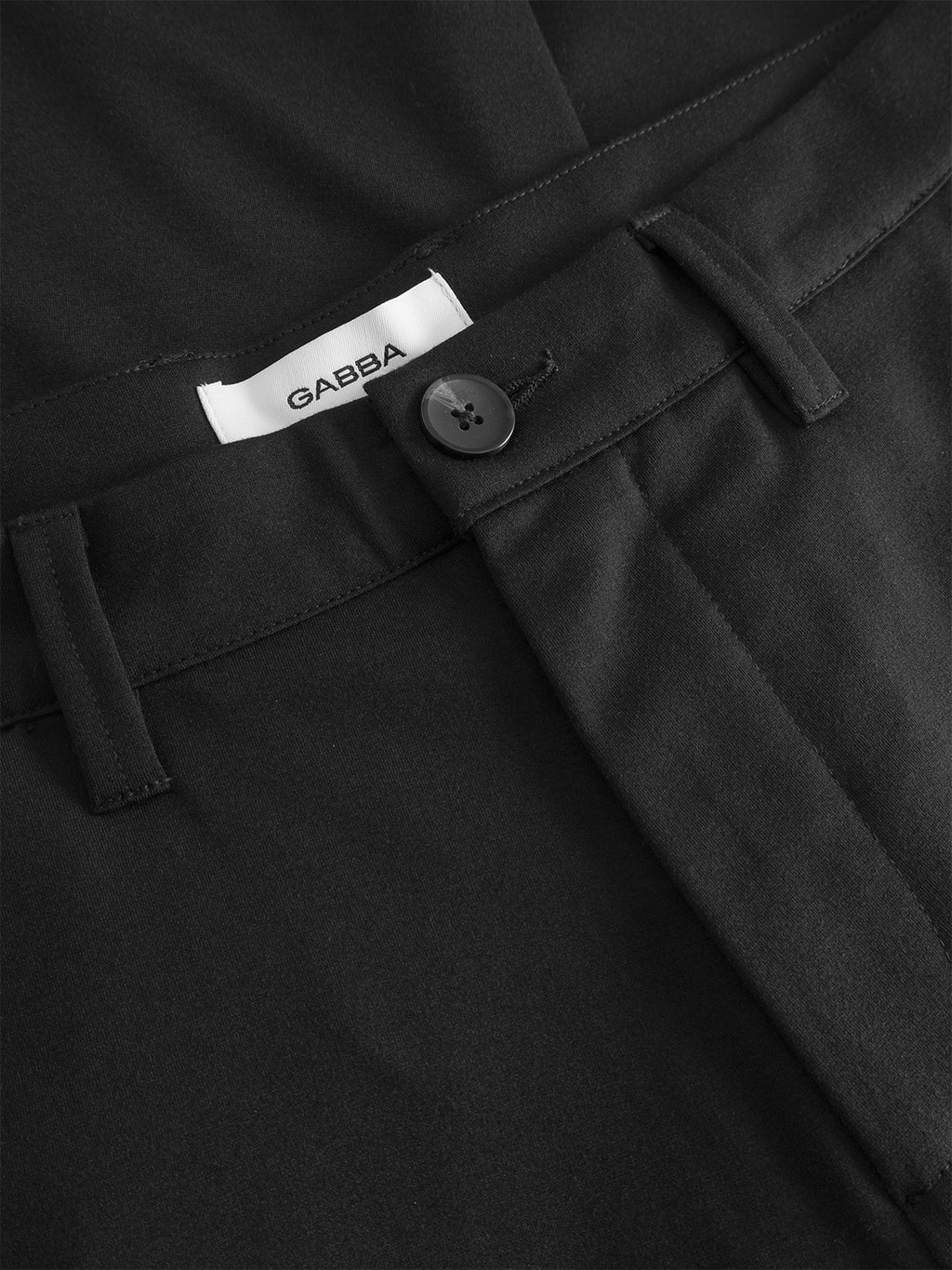 Close-up of the waistband of GABpaul Nygo - Black slim straight fit trousers by Gabba, featuring a single black button, belt loops, and a white Gabba label. Crafted from a viscose blend for stretch comfort.