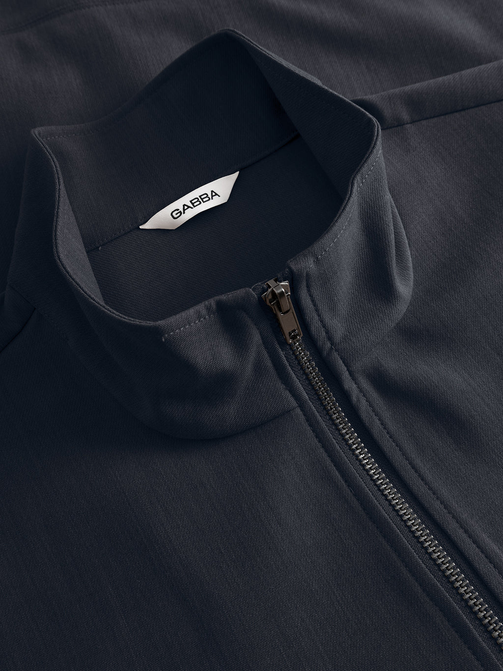 Close-up of the Gabba GABnik Phin GRS jacket in Blue Black, a regular fit zip-through style with a high collar, visible zipper, and white GAEBA label. Made from recycled polyester for a smooth, slightly textured look.