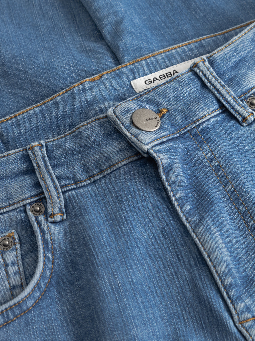 Close-up of GABjones Dhera Jeans in light blue denim, showcasing a slim straight fit with a metallic button, belt loops, classic pockets, and a visible Gabba fabric tag on the waistband. Made from superstretch denim for optimal comfort and style.
