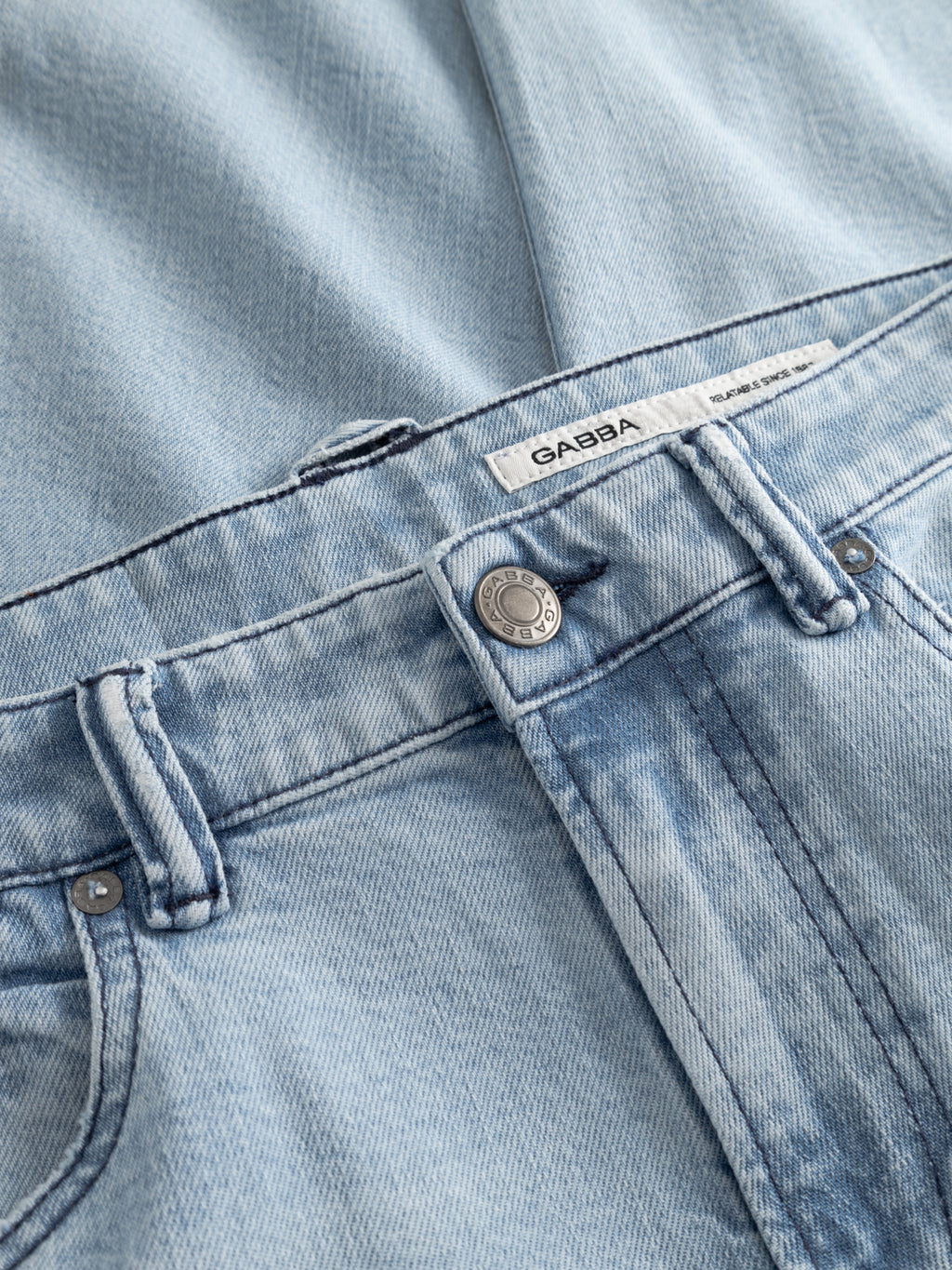 Close-up of GABcarl Swif Jeans by Gabba in light blue bleached denim, highlighting the waistband, belt loops, button, zipper area, and a white brand label.