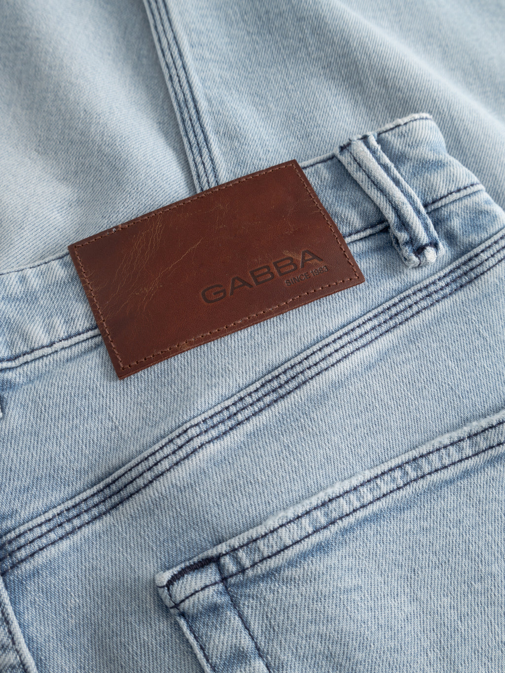 Close-up of GABcarl Swif Jeans in light blue denim by Gabba, made from comfort stretch fabric. Features a brown embossed leather patch above the back pocket, classic stitching, belt loops, and a light bleached finish.
